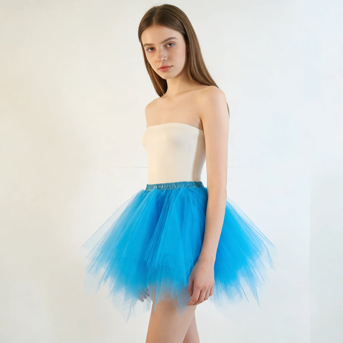 A young woman models a strapless white top and a voluminous, bright blue tulle tutu skirt.