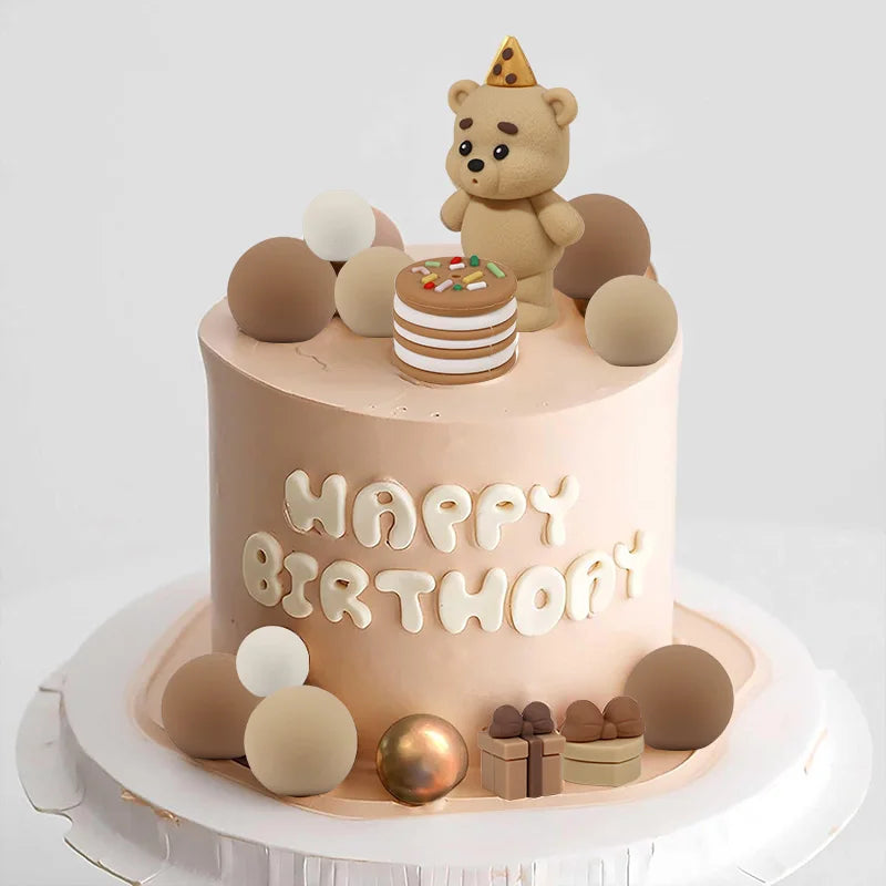 A round cake decorated with a teddy bear topper and various round edible decorations on a white stand.