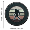 A round, dark brown embroidered patch featuring a silhouette of Bigfoot in white and gray fur against a beige background.