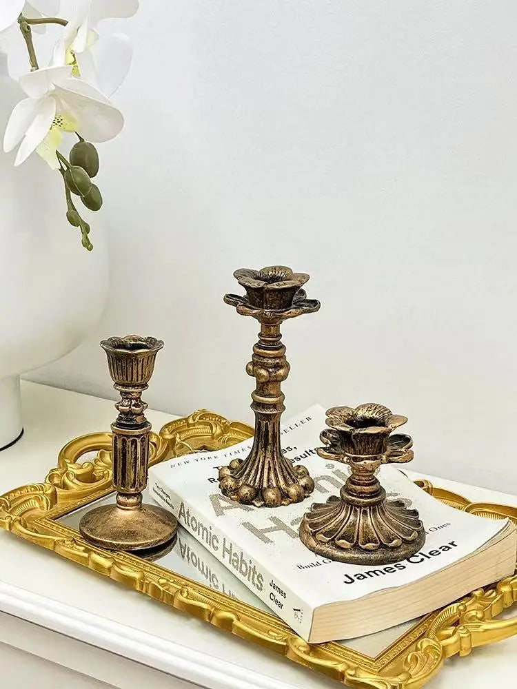 A vintage resin wall sconce candle holder with an ornate bronze base rests on a gold-framed tray next to a book.