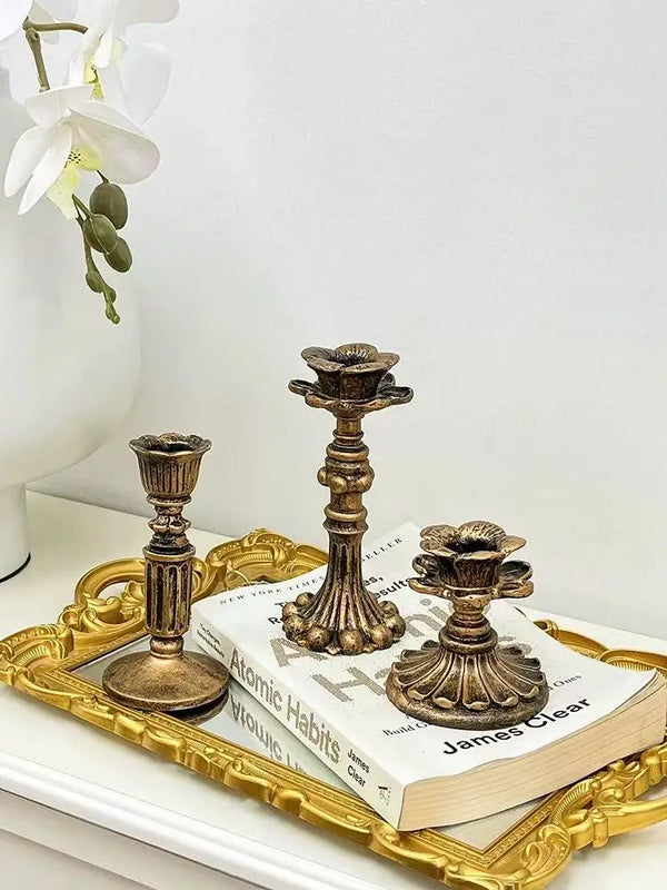 A vintage resin wall sconce candle holder with an ornate bronze base rests on a gold-framed tray next to a book.