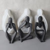 Three abstract silicone molds shaped like seated figures in matte gray and white.
