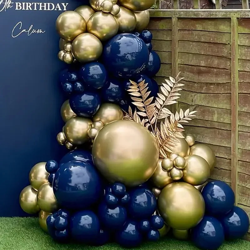 A vertical balloon garland arch featuring navy blue and gold metallic balloons against a wooden background.