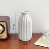 A white ceramic bud vase with vertical ridges is shown on a wooden surface.