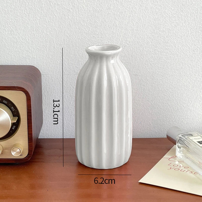 A white ceramic bud vase with vertical ridges is shown on a wooden surface.