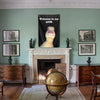 A decorative crib flag hangs on a dark background above a fireplace mantel in a room with wooden furniture and framed picture