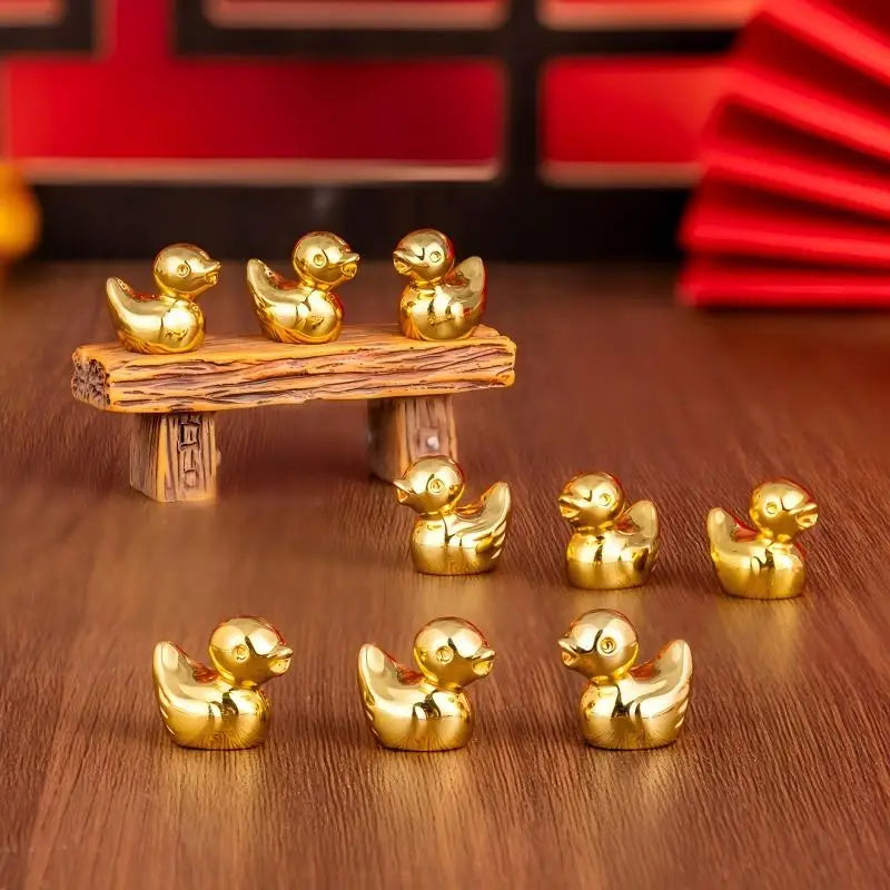 A set of small golden duck resin statues arranged on a wooden plank and surface.