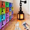 A vertical display of 16-color RGB pixel lanterns used as a night light, next to a black adjustable lamp and a hand holding a