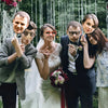 A bride and groom posing with custom face photo props on sticks during a wedding celebration.