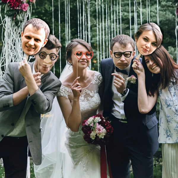 A bride and groom posing with custom face photo props on sticks during a wedding celebration.