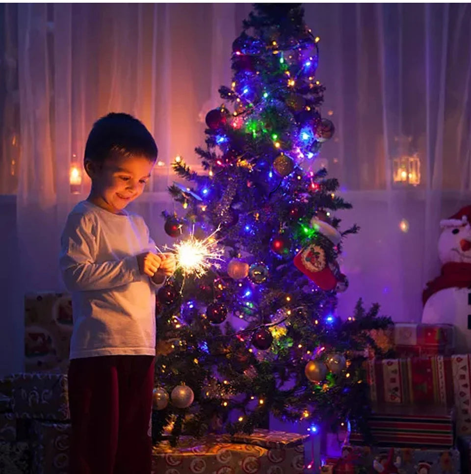 A young boy stands next to a brightly lit Christmas tree decorated with colorful lights and ornaments.