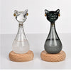 A glass bottle decoration shaped like a cat, featuring a clear and dark green body on a wooden base.