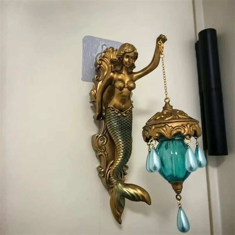 A vintage bronze resin sculpture of a mermaid with flowing hair and a glass lamp pendant hanging from her tail.