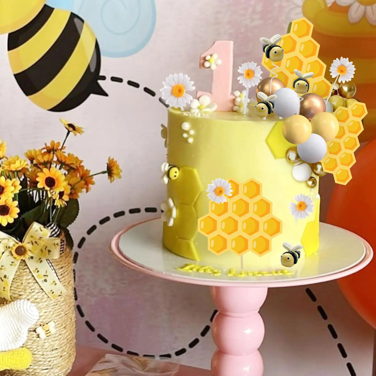 A yellow birthday cake decorated with honeycomb shapes, a number one topper, and small bee figures on a pink stand.