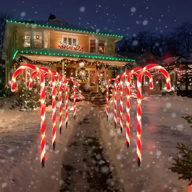 Red and white candy cane shaped solar pathway lights illuminating a snowy path leading to a house at night