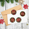A stack of festive Christmas wreath stickers on a white card against a kraft paper envelope with pine greenery.