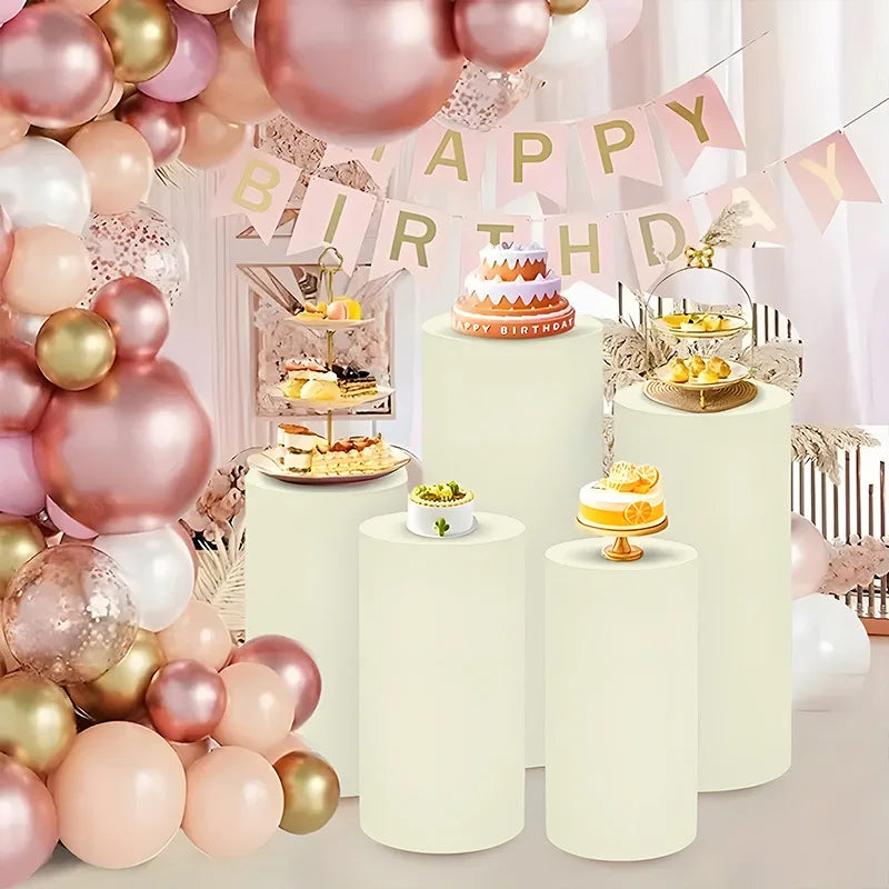 White cylinder stands decorated with pink and gold balloons and party banners for event decor