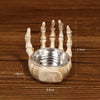A handcrafted resin skull candle holder decoration with a small silver bowl and five fingers, shown on a wooden surface.