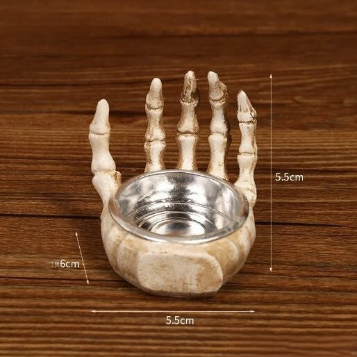 A handcrafted resin skull candle holder decoration with a small silver bowl and five fingers, shown on a wooden surface.