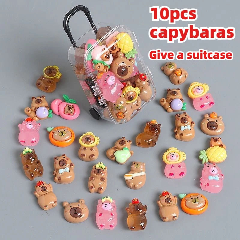 Ten small capybara figures in various colors and textures displayed around a clear plastic suitcase.