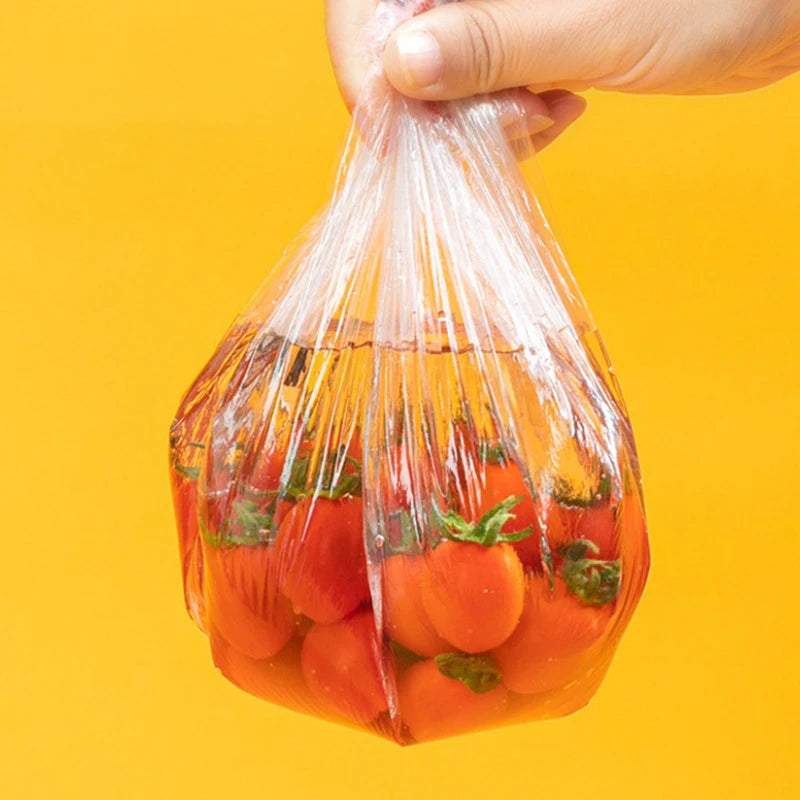 A hand is placing reusable elastic food covers over a bowl filled with fresh tomatoes.