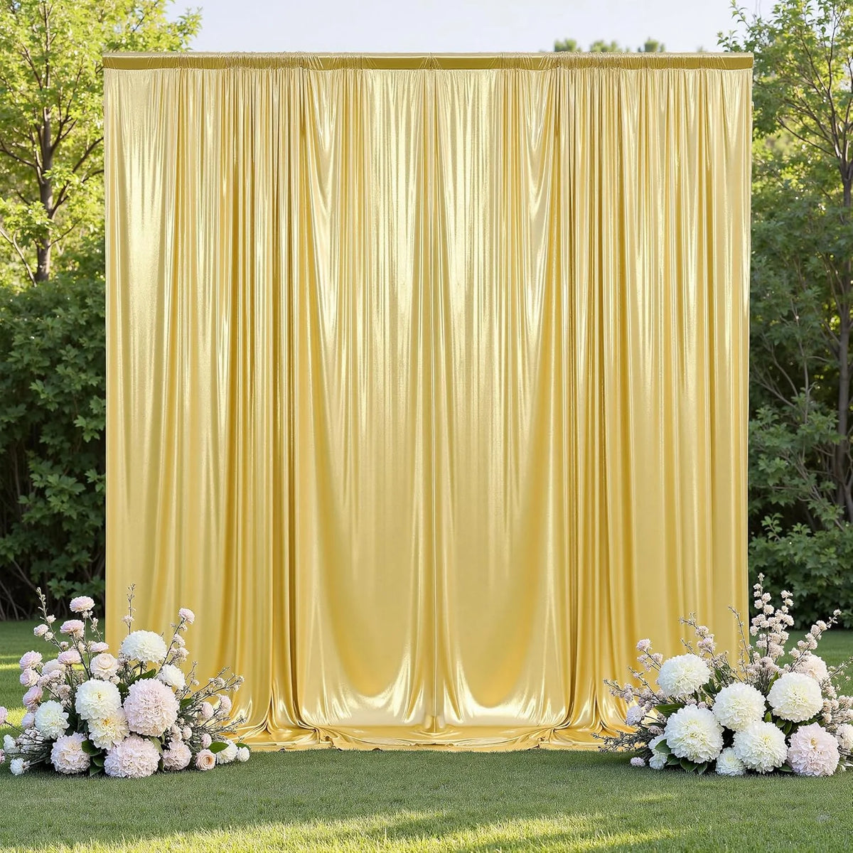 A tall, shimmering gold satin curtain backdrop set up outdoors on a grassy area.