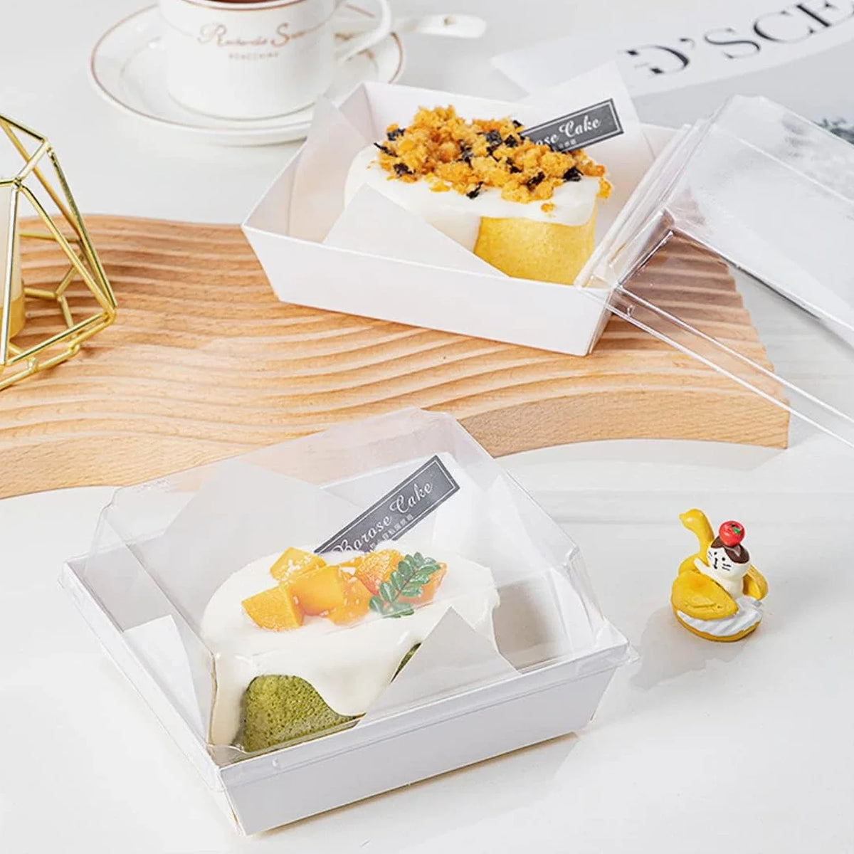 A clear lidded paper sandwich box containing a slice of lemon cake topped with orange zest and mint leaves.