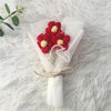 A bouquet of handcrafted red and yellow crochet sunflowers wrapped in white paper and tied with twine