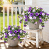 Purple and white artificial petunia bundles displayed in pots on a wooden deck.