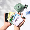 A hand holds a green mini film frame displaying an instant photo, with several other colorful frames nearby.