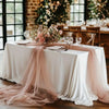 A white draped table setting with pink tulle fabric and floral arrangements in a rustic indoor venue.