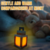 An orange pixel lantern night light rests on a surface next to a sleeping person and a teddy bear.