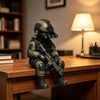 A detailed resin collectible statue of a tactical sniper soldier in olive green armor sitting on a wooden desk.