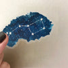 A blue watercolor decal of a constellation with white stars on a transparent sheet.