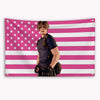 A person wearing a dark shirt stands in front of a pink and white striped American flag banner.