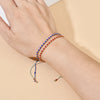 A hand wearing a stack of handmade boho glass bead bracelets with adjustable cords on a light beige background.