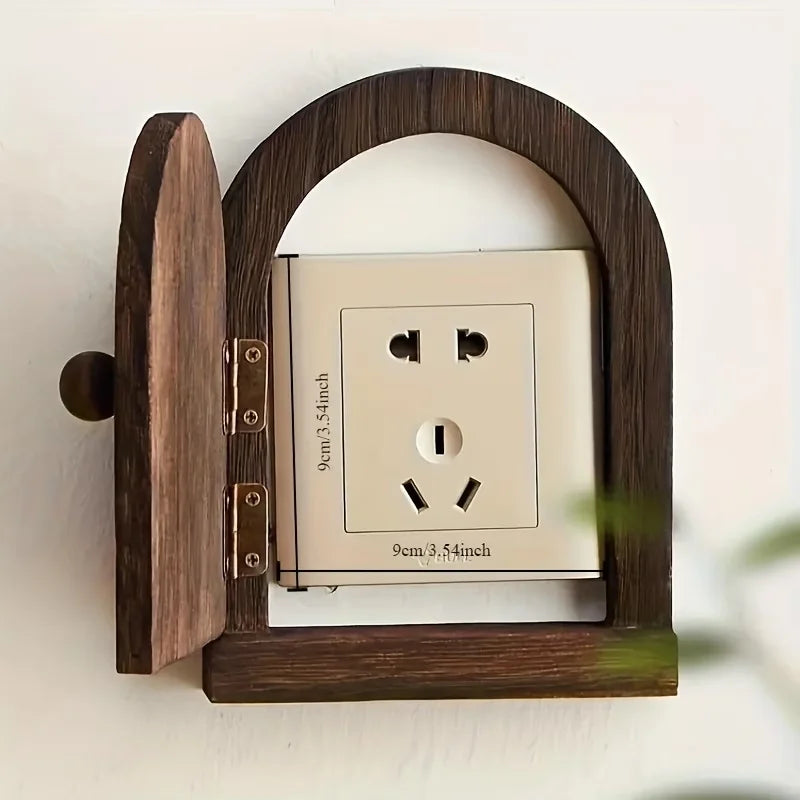 A wooden frame holds a white electrical outlet cover with three prongs.