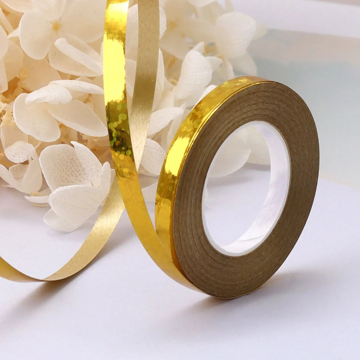 A roll of gold satin balloon ribbon is shown next to white flowers.