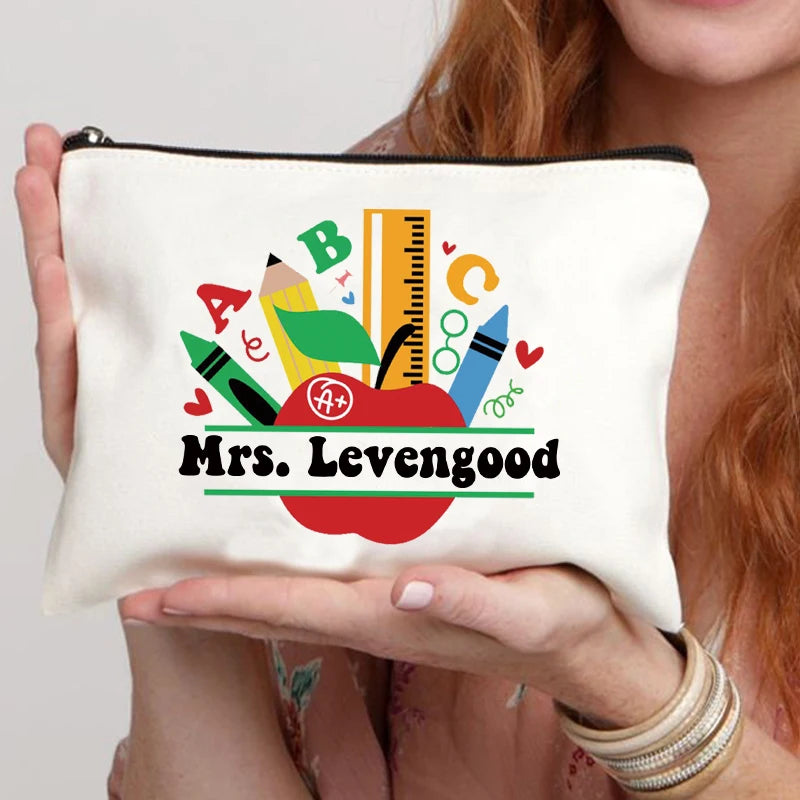 A white canvas makeup bag featuring a design with letters, a ruler, and an apple, with the text Mrs. Levengood.