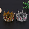 A pair of miniature crown-style tiara jewelry, one gold and one silver, displayed on a dark surface.