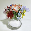 Handcrafted blue glass flower sculpture featuring various colored petals and stems in a clear glass vase.