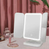 A white tri-fold LED makeup mirror with bright illumination is displayed on a table.