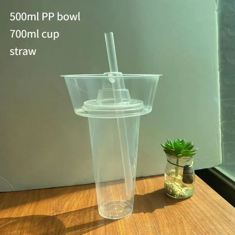 A clear plastic cup with a lid and straw is shown on a wooden surface.