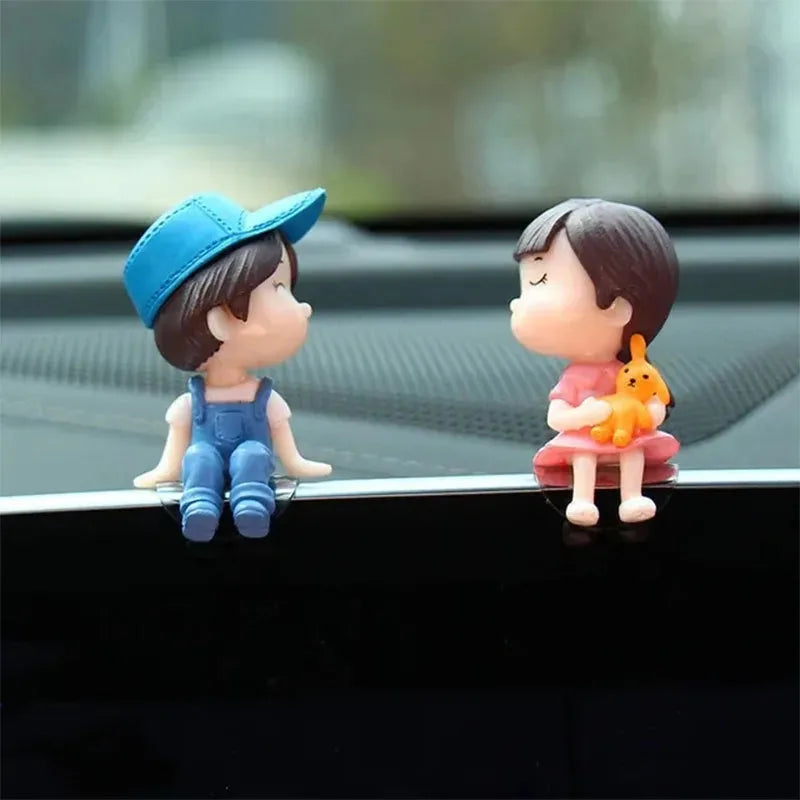 A cute figurine of a couple with a balloon sitting on a black car dashboard.
