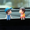 A cute figurine of a couple with a balloon sitting on a black car dashboard.