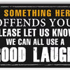A black metal sign with yellow text that reads If something here offends you please let us know we can all use a good laugh