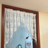 A large mirror framed in wood features a sheer white beaded lace valance curtain hanging over the top.