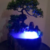A resin waterfall desktop fountain with a dark base and illuminated blue LED lighting featuring green foliage.