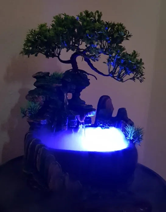 A resin waterfall desktop fountain with a dark base and illuminated blue LED lighting featuring green foliage.