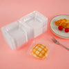 A clear plastic box with a lid containing a piece of glazed cake on a pink background.